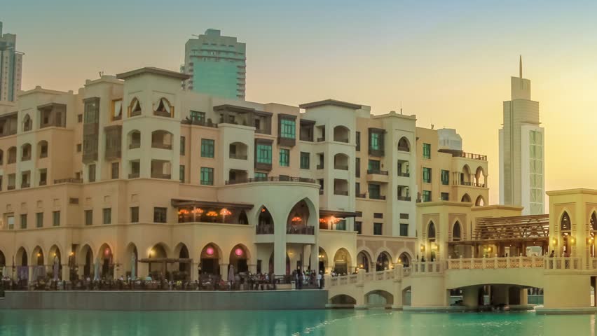 Scenic view of Burj Khalifa Lake, a pool where they dance the Dubai Fountain. On background, the bridge that connects the Dubai Mall to Souk Al Bahar. People crowd around the shopping area at sunset.