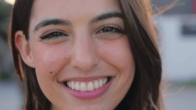 Close-up of face of beautiful young Caucasian woman posing smiling with mole on cheek. Pleasant white girl standing cheerful outdoors. Attractive happy pretty female looking joyful at camera