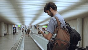 Caucasian young adult man with backpack using mobile phone standing on escalator conveyor of airport corridor. European people concentrating typing digital device for travel in transportation concept  - Powered by Shutterstock - Get 15% off with code: PIKWIZARD15