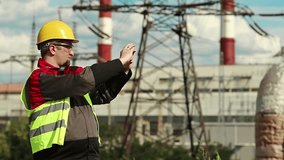 Powerman records videos on smartphone. Worker in yellow hard hat with smartphone at electric power plant