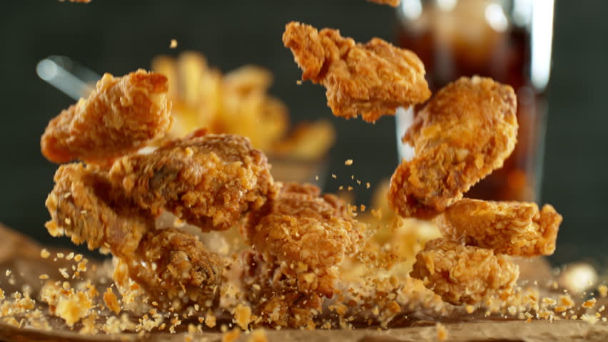 Super slow motion of flying fried chicken pieces with french fries and cola drink. Filmed on high speed cinema camera, 1000fps, placed on high speed cine bot. Camera in motion, following objects.