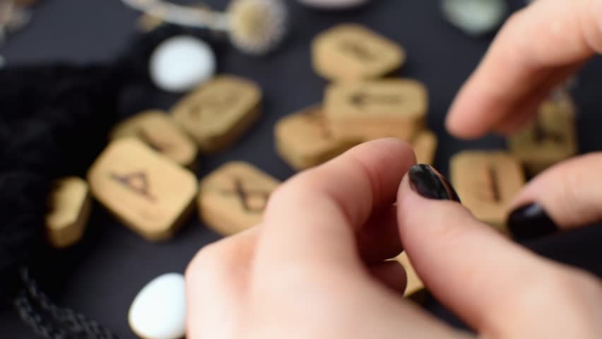 Scandinavian wooden runes in the hands of a fortune teller on a black table with velvet bags and stones. Magic esoteric symbols and signs for divination and prediction of the future and fate.