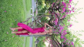 Vertical Video. Charming Young Asian Girl in Pink Long Dress Posing Near a Blooming Tree. Beautiful Woman Standing Near a Tree and Smelling Flowers. People Concept