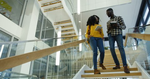Young African American couple of students going down the stairs at the college after the classes and talking. Man asking a woman about a date. Indoor
