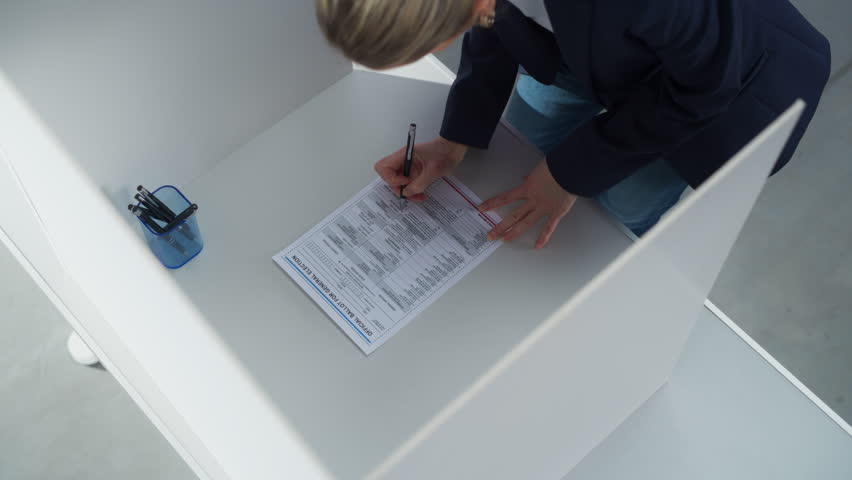 Female Filling Out a Paper Ballot in a Voting Booth on the Day of Presidential Elections in the United States of America. Anonymous Woman Choosing to Vote for Elected Officials. Top Down Footage