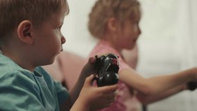 Focused toddler and preschooler control consoles playing video game on blurred background. Adorable children sit on sofa enjoying competition closeup