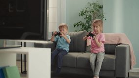 Toothless blonde girl jumps feeling proud and happy to win video game playing with little brother. Happy preschooler and sad boy in living room