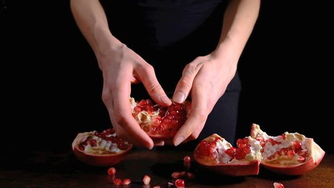 Female hands peeling a pomegranate on a dark background, pomegranate seeds falling on table in slow motion in 4k.