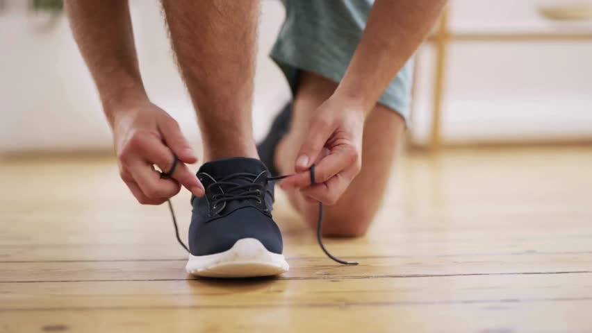 Young man tying shoelace on sport shoes indoors, closeup shot. Closeup of man tying shoelaces on his sneakers. Athlete tied up shoelaces of his running shoes before exercising. Royalty-Free Stock Footage #3424625159