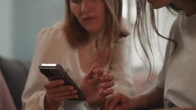 Blonde woman shows baby photos to girlfriend on smartphone on blurred background. Soulmates share moments and memories at home closeup