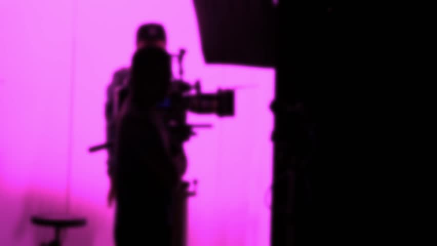 Blurry silhouette footage of film or video production which camera operator director and film crew working in studio set. Behind the scene of filming movie that film crew setting camera and monitor.