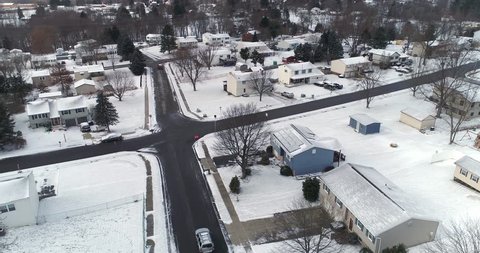 A daytime winter overcast aerial establishing shot of a typical Western Pennsylvania residential neighborhood and intersection. Slow forward motion. Snow covered roofs, houses, and yards.