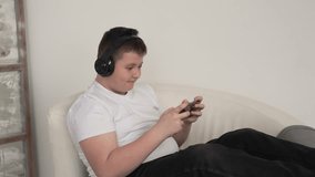 Happy man gamer wearing headphones competition playing video games online with smartphone in modern house. Streaming online eSports game, home quarantine.