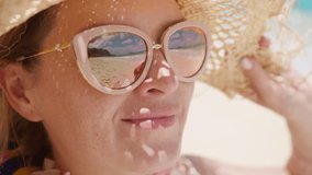 Portrait of beautiful caucasian woman smiling, looking at stunning tropical ocean beach. Close up woman face in straw hat and golden sunglasses enjoying island views. Happy traveler female enjoys life