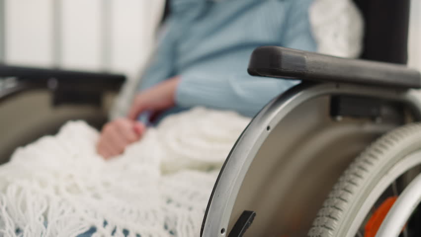 Cheerful little girl shows thumb up gestures sitting in wheelchair on blurred background. Schoolgirl with disability smiles looking in camera closeup Royalty-Free Stock Footage #3424768505