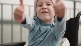 Cheerful little girl shows thumb up gestures sitting in wheelchair on blurred background. Schoolgirl with disability smiles looking in camera closeup - Powered by Shutterstock - Get 15% off with code: PIKWIZARD15