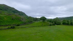 AERIAL: Strong wind blows through picturesque green valley in Lake District, United Kingdom. Beautiful countryside with meadows, fenced with stones, and a small streams winding into a ribbon lake. - Powered by Shutterstock - Get 15% off with code: PIKWIZARD15