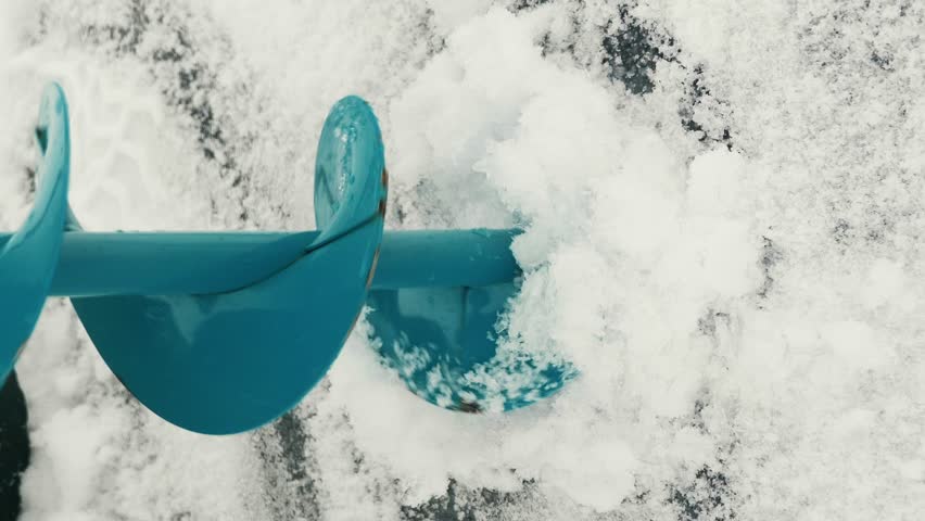 Ice drill is making ice hole in frozen river. Fisherman is drilling ice hole with ice drill in hands. Winter fishing. Vertical video