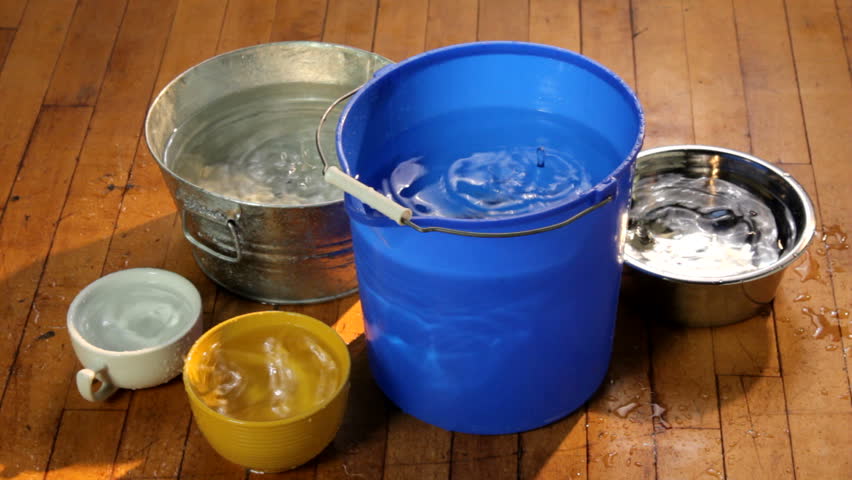 Water dripping from a leaking ceiling into colorful buckets and containers on