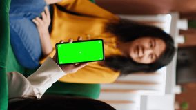 Vertical Video Customer looking at greenscreen layout on phone display, waiting for check in at hotel. Asian woman sitting on couch with smartphone showing blank copyspace mockup layout. Tripod shot.