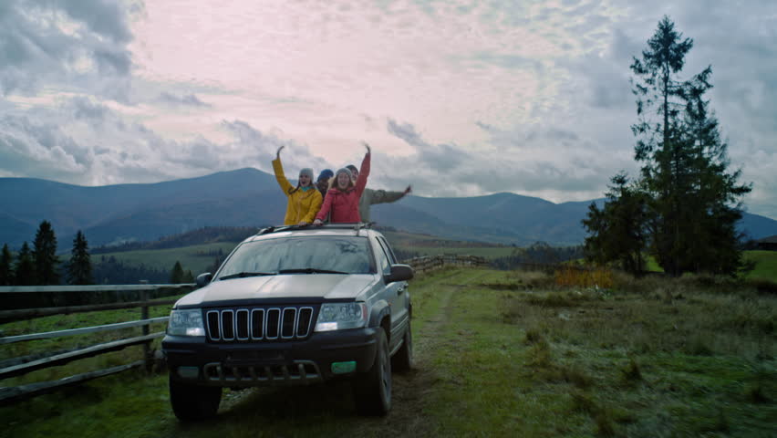 Group of diverse tourists together ride on vacation in mountains. Hikers standing up through sunroof of car, laugh and wave hands on road trip. People having fun on the car trip. Outdoor enthusiasts. Royalty-Free Stock Footage #3424869327