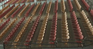 Drone, aerial, video of old faded orange and yellow painted wooden seats at a abandoned a stadium grandstand.
