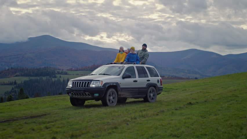 Group of tourists together ride on vacation in mountains. Hikers standing up through sunroof of car dance and wave hands on road trip. People enjoy drive in car hatch. Outdoor recreation. Slow motion. Royalty-Free Stock Footage #3424926389