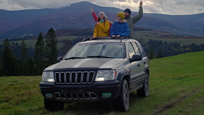 Group of travelers together explore mountains. Hikers standing up through sunroof of car laugh and enjoys drive on road trip. Outdoor enthusiasts having fun on car trip. Tourism concept. Slow motion. Royalty-Free Stock Footage #3424935043