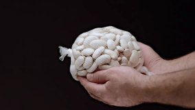A nylon bag filled with white beans being playfully flipped in hands, the slow-motion video emphasizing the visible beans.