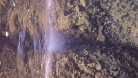 Vertical footage, Close-up of sea waves crash against cliff, penetrating crack and filling it with small air bubbles, Slow motion. Marine waves crashing on coastal rock reef