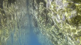 Vertical footage, Camera moving forwards underwater along cliff on bright sunny day in sun glare, Slow motion. Underwater landscape of Mediterranean Sea, Greece