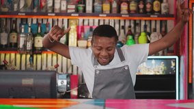 Happy barman dances at club countertop. Joyful African American bartender shows peace gesture in nightclub at party. Black waiter has fun at work - Powered by Shutterstock - Get 15% off with code: PIKWIZARD15