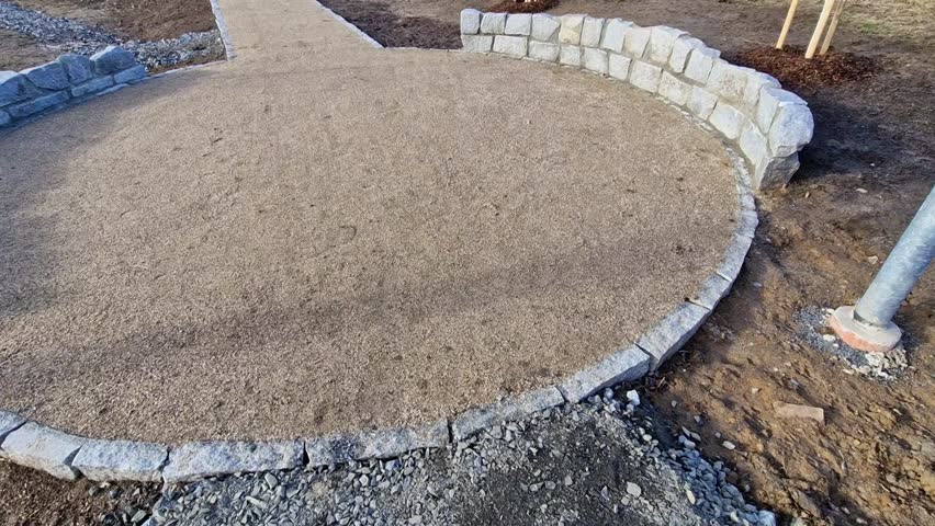 circular rest stop with an obelisk at the end of path in the park. bounded by stone wall in an arch along edge of the area. stones border tree which is protected against damage from impact, dog urine 