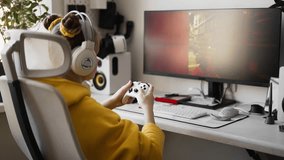 Teenage girl with headset is sitting in a comfortable computer chair, holding a white gamepad in her hands and playing a game on a PC or console. Slow motion shooting.