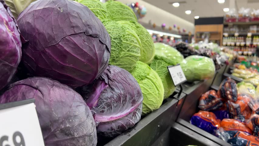 Cabbage close-up on a blurred store background. Red cabbage close-up. A Caucasian woman 50-55 years old chooses two heads of Savoy cabbage. Savoy cabbage is a source of protein and mineral salts