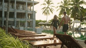 Young couple in swimsuits walking along swimming pool of luxury resort hotel on ocean shore. Cheerful girl and guy holding hands near swimming pool. Happy two people relax on poolside together. - Powered by Shutterstock - Get 15% off with code: PIKWIZARD15