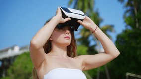 Woman dons VR headset, exploring immersive tropical beach environment. Engages with digital realm, palm trees sway, embodying metaverse presence, AR tech binds real and virtual worlds. Slow motion. - Powered by Shutterstock - Get 15% off with code: PIKWIZARD15
