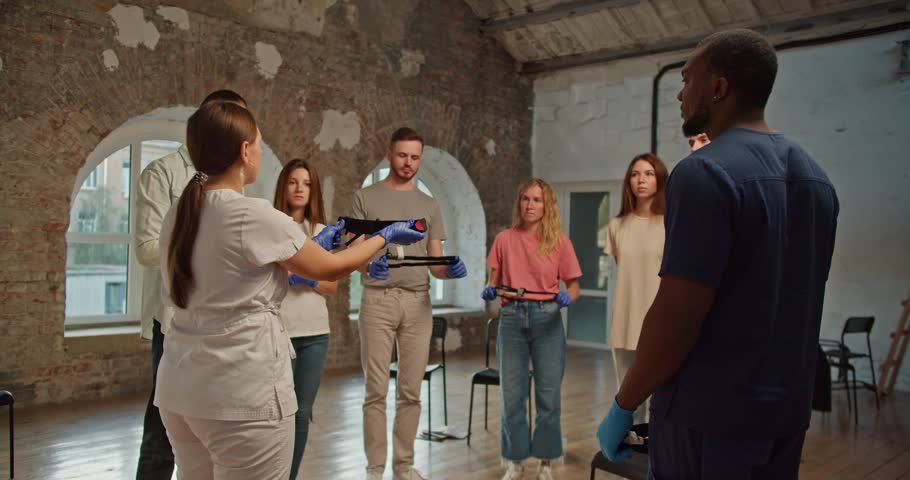 Shooting behind the shoulders: A professional female doctor in a medical white uniform, together with a Black man assistant in a blue medical uniform, conduct a medical training course, talking about Royalty-Free Stock Footage #3425297319
