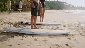 Travelers couple take and carry surfboards on sandy beach, go towards water. Man, woman pick up, walk with rented boards to lineup ocean waves. Tourists start surfing session at tropical spot. No face - Powered by Shutterstock - Get 15% off with code: PIKWIZARD15