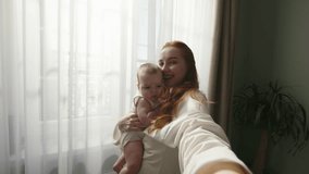 Mom blogger making video with baby. Young modern woman holds phone in hand, shoots video, takes photo with baby child for social networks. Lifestyle blog of young mother about life and upbringing.