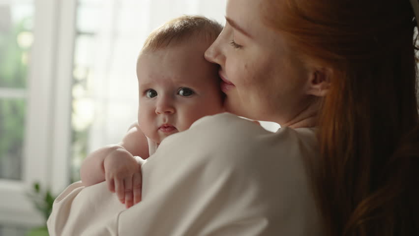 Child in mother arms, pleasure and happiness. Woman mother kisses, caresses, hugs child, holds in arms. Portrait of laughing baby kid toddler in arms of mother. Baby kid boy or girl, mom hugging baby Royalty-Free Stock Footage #3425317335