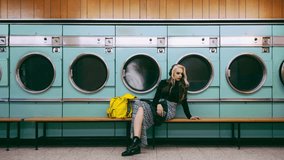 Laundromat for clothes, woman waiting and cleaning service with fashion, style and listening to sad music by washing machine. Young, trendy person or retro model by vintage laundry or spinning effect - Powered by Shutterstock - Get 15% off with code: PIKWIZARD15