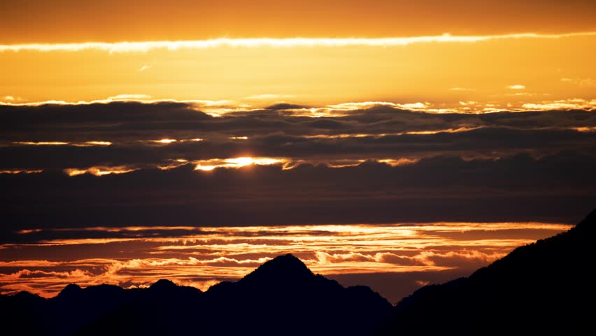 Silhouettes of mountains in golden sunset. Moving clouds in orange sky. Warm winter mountain scenery in northern Taiwan, Shuangxi Buyanting Pavilion.