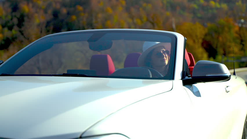 Succesful relaxed woman driver touches steering wheel sitting in convertible car. She is enjoying her life, , view through windshield. Tourism, road trip, journey, vacation, travel, car trip concept.