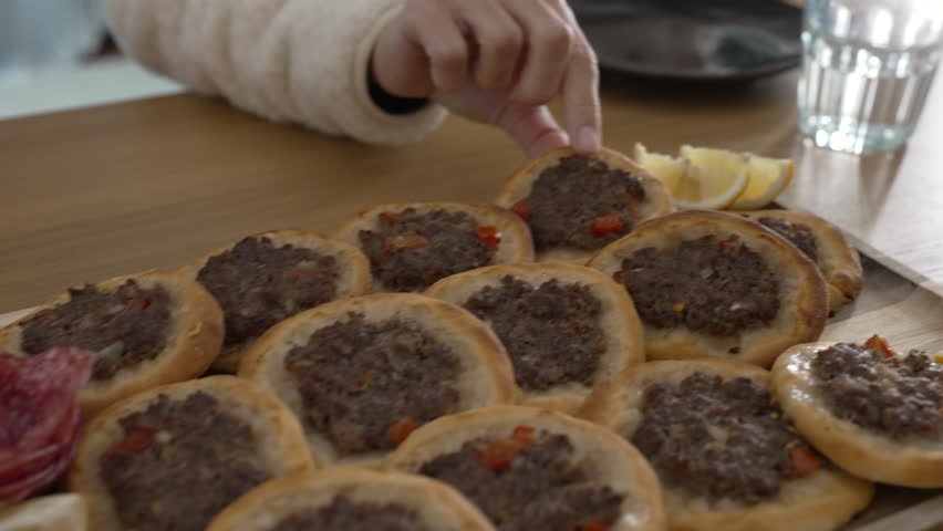 Woman grabbing an esfiha from plate during mealtime. Person snacking traditional Arabic Brazilian food