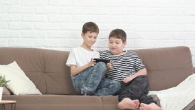 Two boys childs sitting on sofa, playing online game, smiling in light living room.
