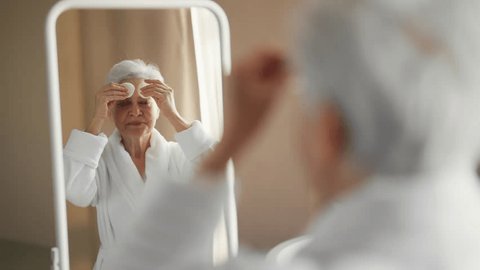 Senior woman doing skincare procedures in bathroom wiping cleansing wrinkled face using cotton pad. Self-care, home spa beauty cosmetics anti-aging practice, wellbeing cleaning peeling concept. ஸ்டாக் வீடியோ