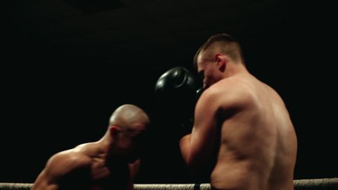 In the boxing ring, the pumped-up bald Boxer conducts a duel with a partner in boxing gloves.
