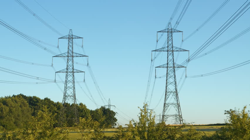High voltage transmission line near a power station in the English countryside. Industrial construction with numerous steel towers and cables for distribution of electric energy along large distances. Royalty-Free Stock Footage #3425436541