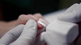 Master applies transparent lacquer on customer nail with small brush in cosmetology salon closeup. Beautician covers woman fingernail with protective product in beauty shop. Manicurist serves client - Powered by Shutterstock - Get 15% off with code: PIKWIZARD15